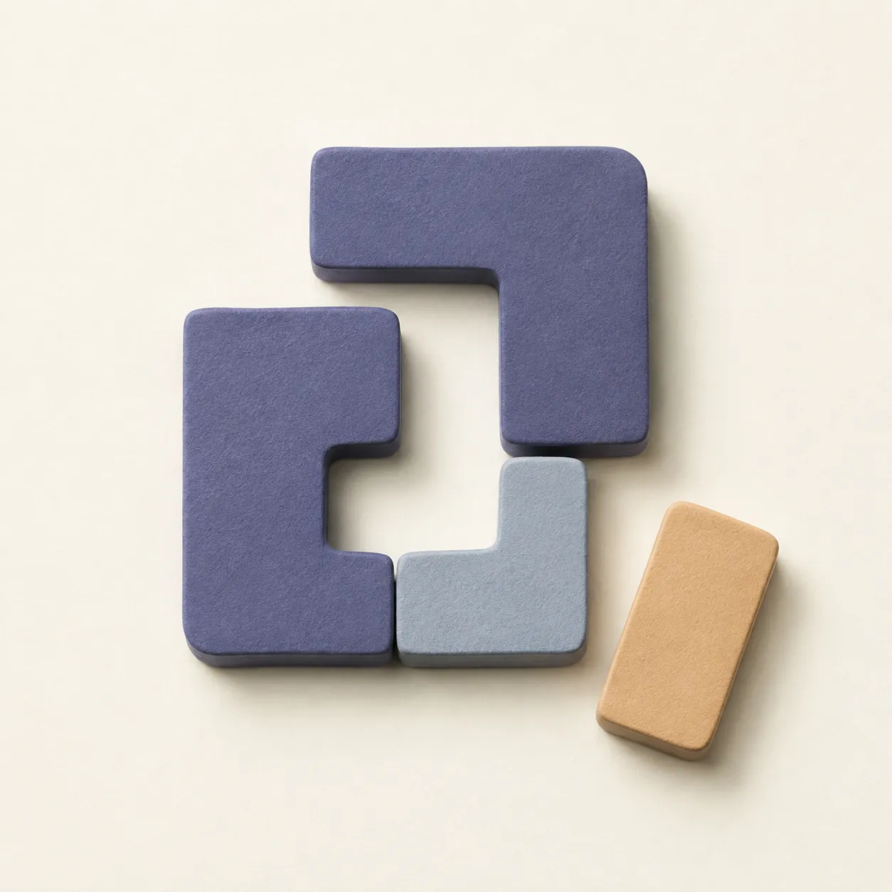 Indigo and mist-blue geometric pieces form an open arrangement on ivory, with an apricot piece waiting beside them.